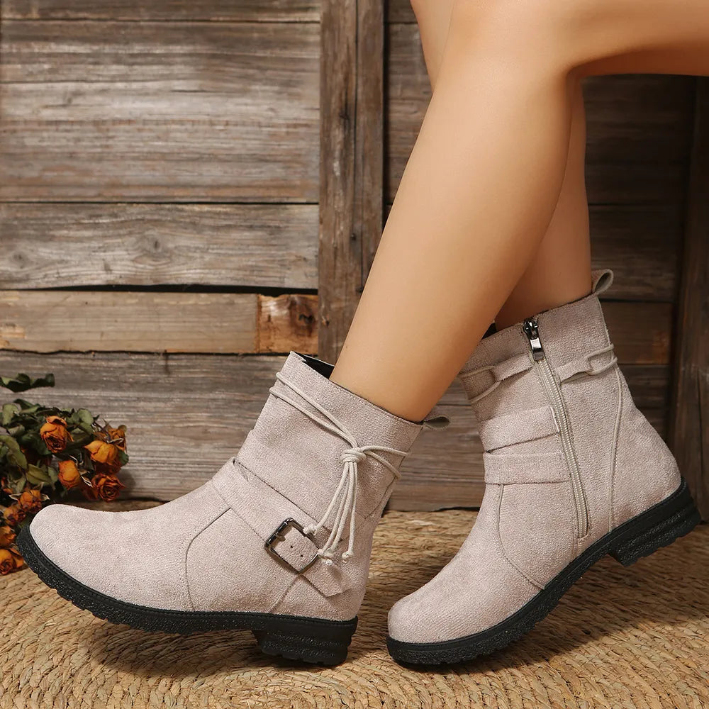 Beige ankle boots with buckles worn by a person against a wooden background