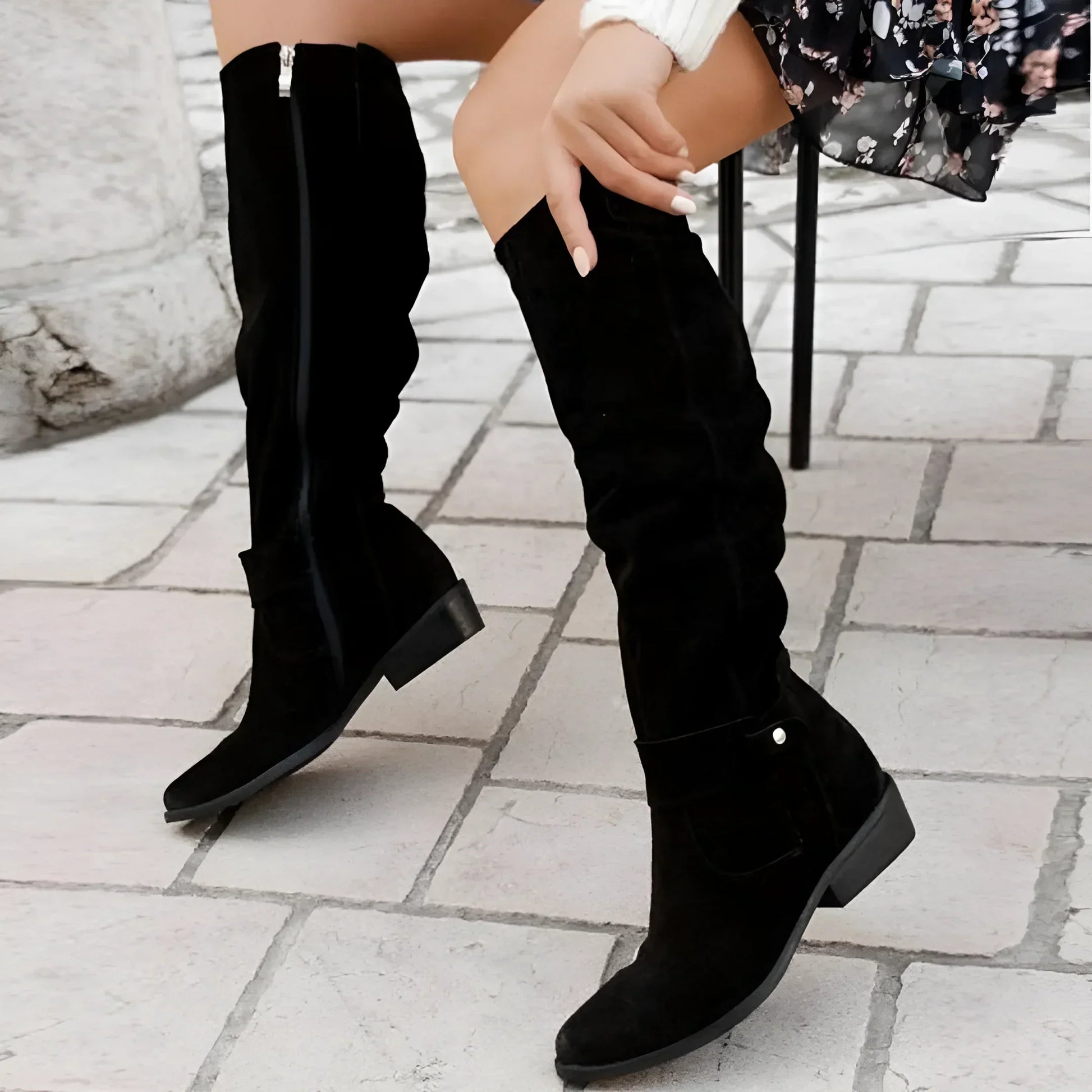 Black knee-high boots worn by a person on a stone pavement