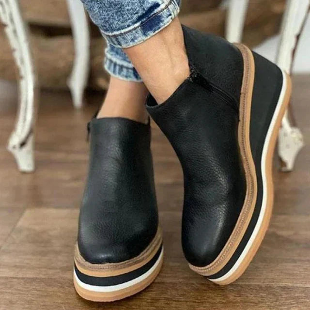 Black platform ankle boots with brown soles worn indoors on a wooden floor