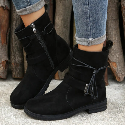 Black suede boots worn with rolled-up jeans against a rustic wooden background