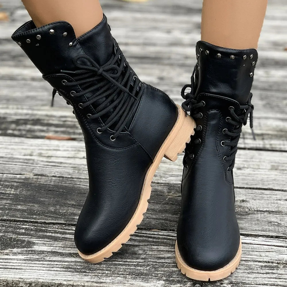 Black vegan leather boots with beige soles on a wooden floor