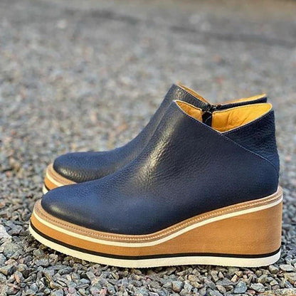 Blue wedge ankle boots with brown soles on a gravel surface