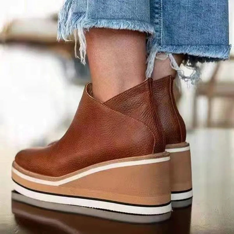 Brown platform ankle boots worn with denim jeans on a blurred background