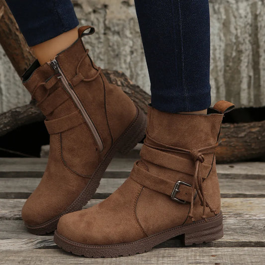 Brown suede boots with buckles worn by a person on a wooden floor