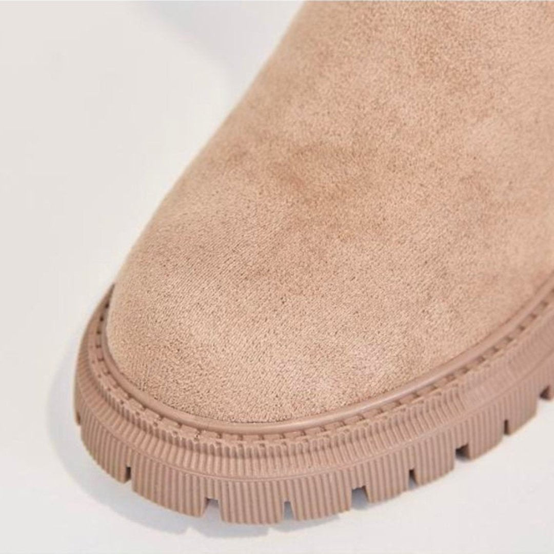 Close-up of a beige suede boot with a white sole on a light gray background