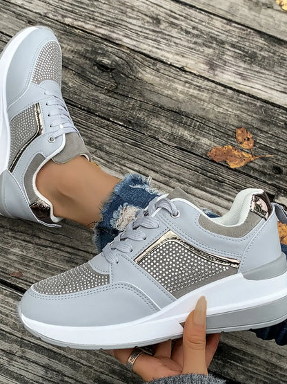 Gray sneakers with rhinestone details held by a hand on a wooden surface