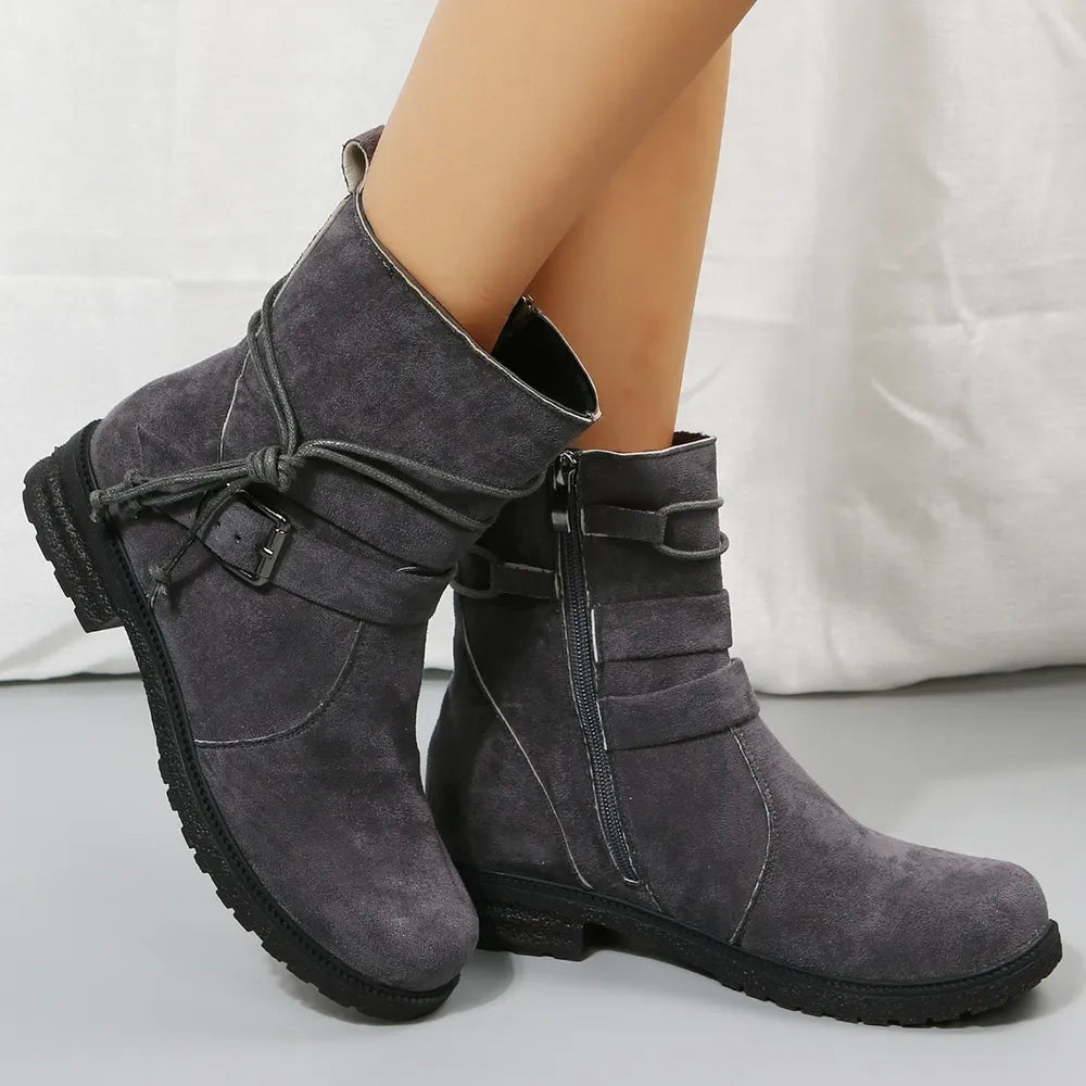 Gray suede boots with buckles worn by a person on a light gray background