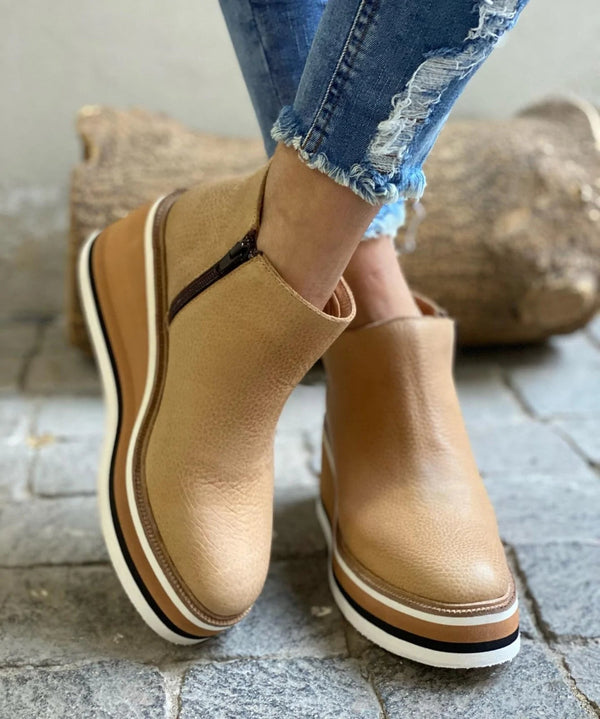 Tan platform shoes worn with blue jeans on a stone floor
