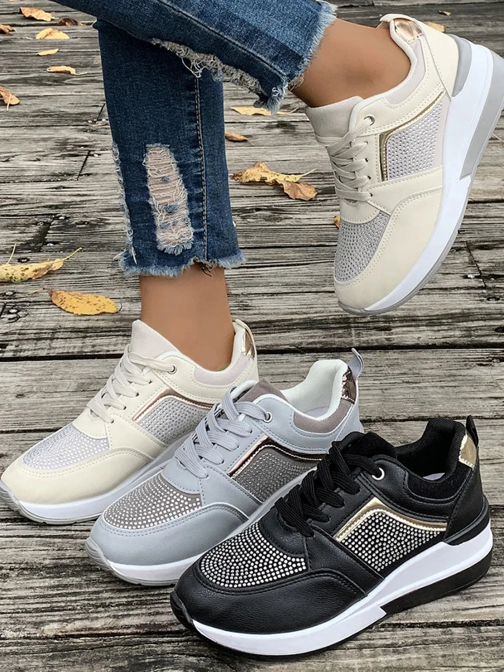 Three pairs of sneakers on a wooden floor with autumn leaves