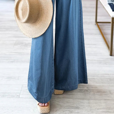 Person wearing blue wide-leg pants holding a straw hat in a store setting